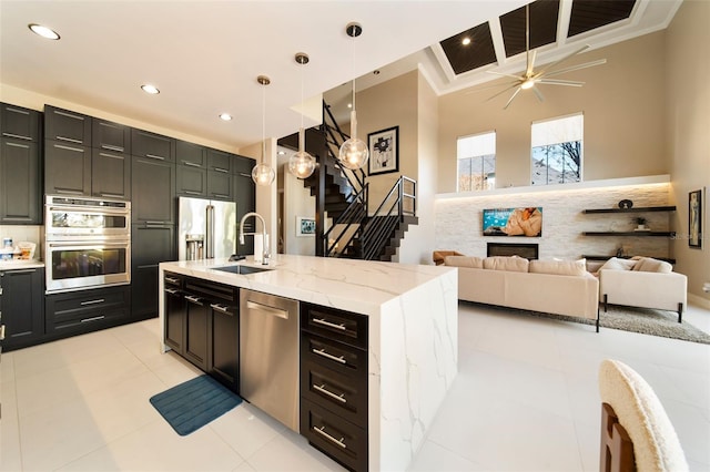 kitchen with light stone counters, pendant lighting, a center island with sink, appliances with stainless steel finishes, and sink