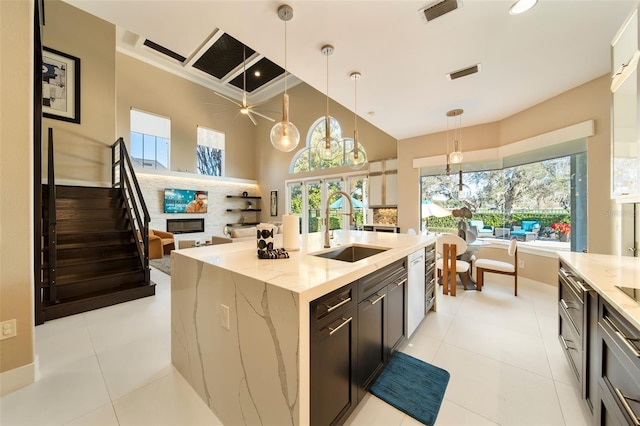 kitchen featuring sink, light stone counters, light tile patterned floors, hanging light fixtures, and a center island with sink