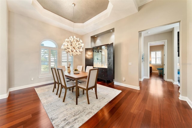 dining space with an inviting chandelier, dark hardwood / wood-style floors, and a tray ceiling