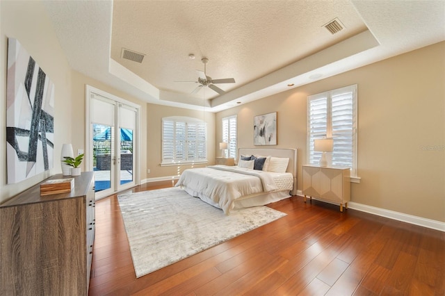 bedroom with ceiling fan, a raised ceiling, a textured ceiling, and access to exterior