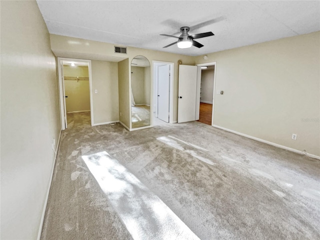 unfurnished bedroom featuring a walk in closet, ceiling fan, a closet, and carpet flooring