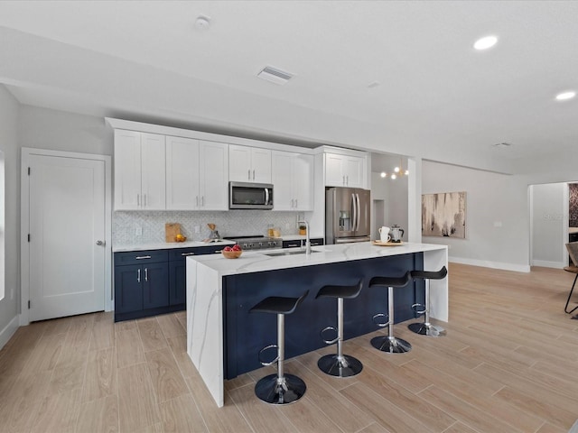 kitchen with a kitchen bar, white cabinetry, an island with sink, and stainless steel appliances