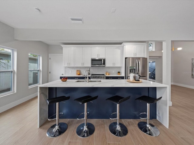 kitchen with appliances with stainless steel finishes, backsplash, a breakfast bar area, light hardwood / wood-style floors, and white cabinetry