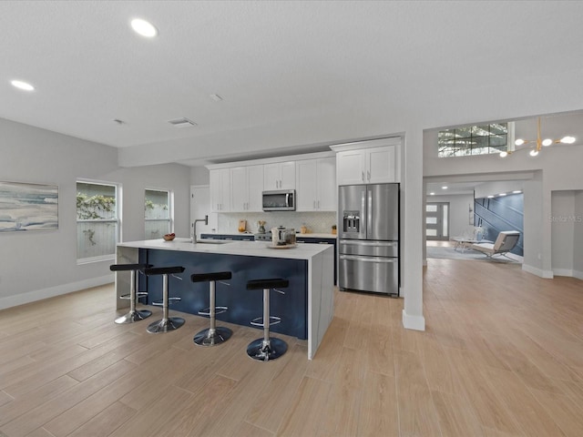 kitchen with a breakfast bar area, stainless steel appliances, white cabinetry, and light hardwood / wood-style flooring