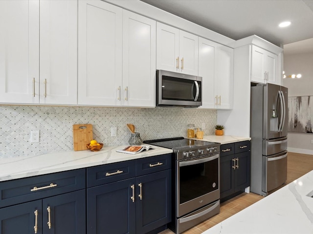 kitchen with appliances with stainless steel finishes, light hardwood / wood-style flooring, backsplash, light stone countertops, and white cabinetry