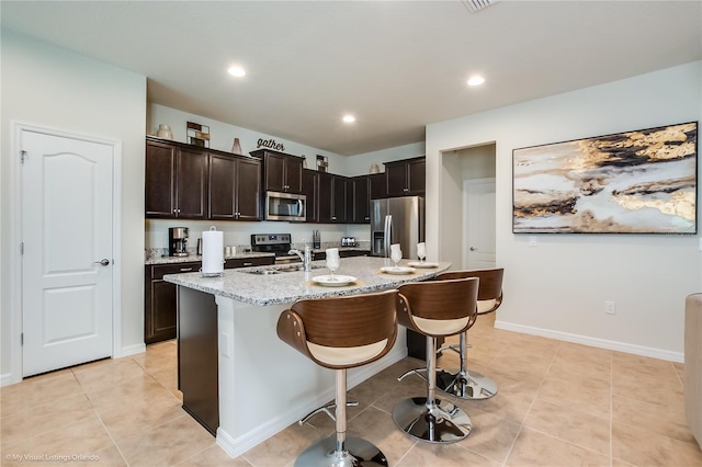 kitchen featuring light tile floors, an island with sink, stainless steel appliances, and a breakfast bar