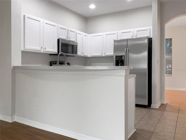 kitchen with kitchen peninsula, tile patterned flooring, white cabinetry, and stainless steel appliances