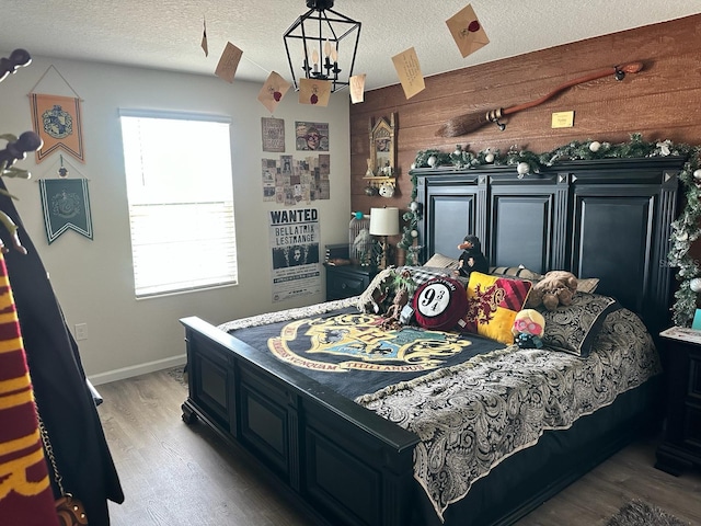 bedroom featuring wood-type flooring, a textured ceiling, a notable chandelier, and wooden walls