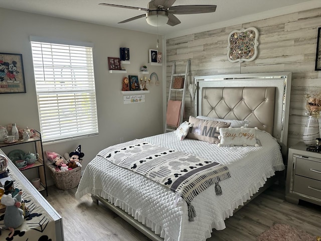 bedroom featuring ceiling fan, wood walls, hardwood / wood-style flooring, and multiple windows