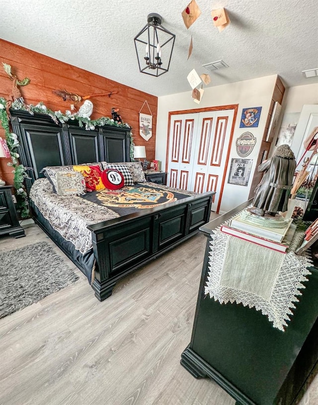 bedroom featuring a chandelier, wood walls, light wood-type flooring, and a textured ceiling