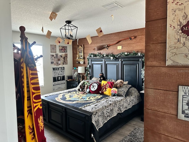 bedroom with wood walls, light wood-type flooring, a textured ceiling, and a notable chandelier