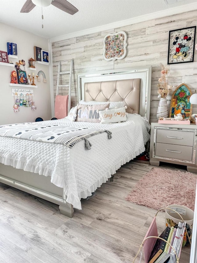 bedroom featuring light wood-type flooring, ceiling fan, wood walls, and a textured ceiling