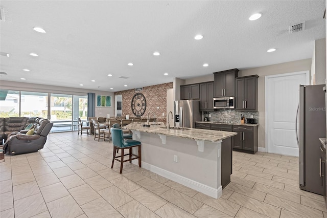 kitchen with light tile floors, light stone counters, a kitchen breakfast bar, appliances with stainless steel finishes, and a center island with sink