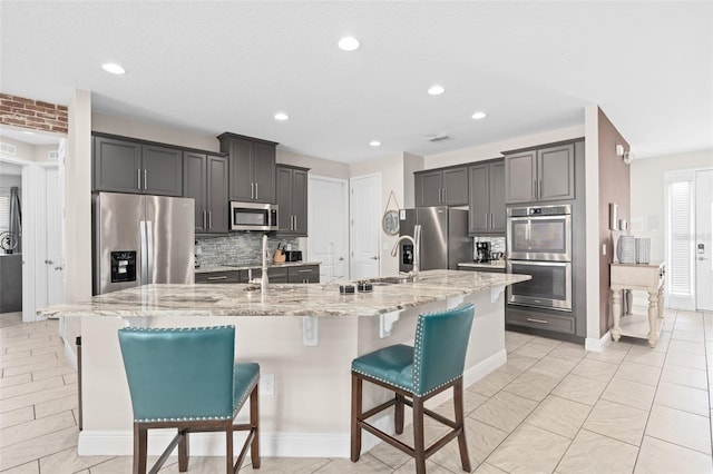 kitchen featuring an island with sink, a kitchen breakfast bar, tasteful backsplash, appliances with stainless steel finishes, and sink