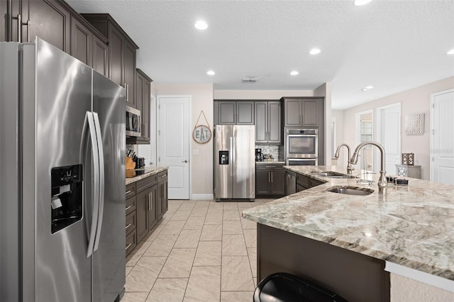 kitchen with light stone counters, appliances with stainless steel finishes, light tile flooring, tasteful backsplash, and dark brown cabinetry