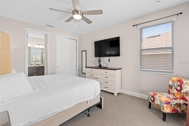 bedroom with a closet, connected bathroom, light carpet, and ceiling fan