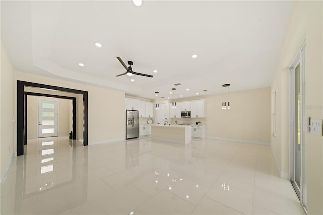 tiled empty room featuring a raised ceiling, sink, and ceiling fan