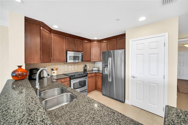 kitchen with stainless steel appliances, light tile floors, tasteful backsplash, dark stone countertops, and sink