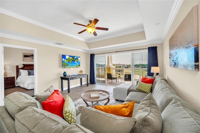 living room with a raised ceiling, crown molding, light hardwood / wood-style floors, and ceiling fan