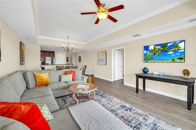 living room featuring ornamental molding, ceiling fan with notable chandelier, a tray ceiling, and light wood-type flooring