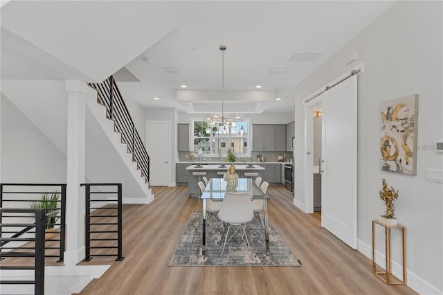 dining room with a barn door, light hardwood / wood-style floors, and an inviting chandelier