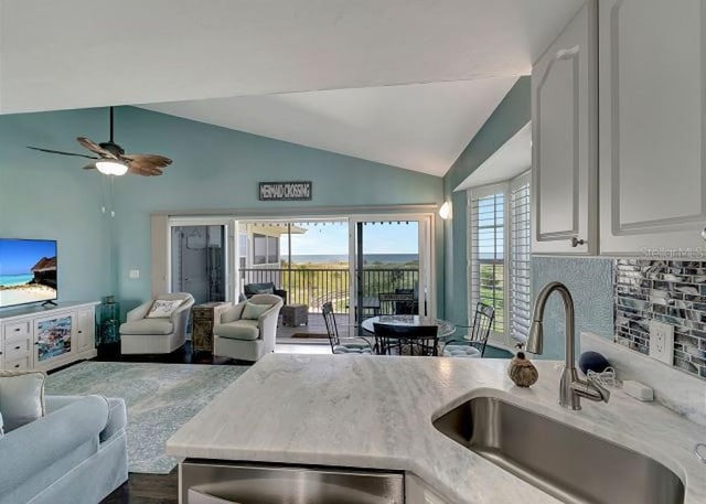 kitchen featuring decorative backsplash, open floor plan, vaulted ceiling, white cabinetry, and a sink