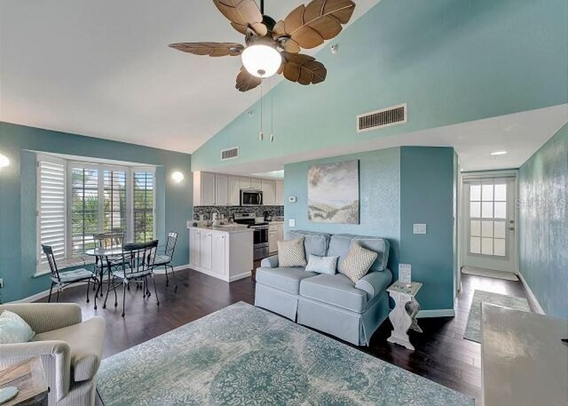 living area with high vaulted ceiling, baseboards, visible vents, and dark wood-type flooring