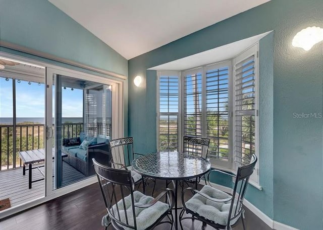 dining area with dark wood-style floors, a textured wall, vaulted ceiling, and baseboards