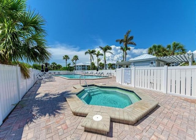 pool with fence, a hot tub, and a patio