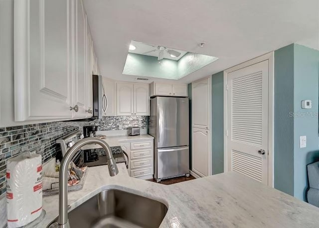 kitchen featuring stainless steel appliances, light countertops, backsplash, white cabinetry, and a sink