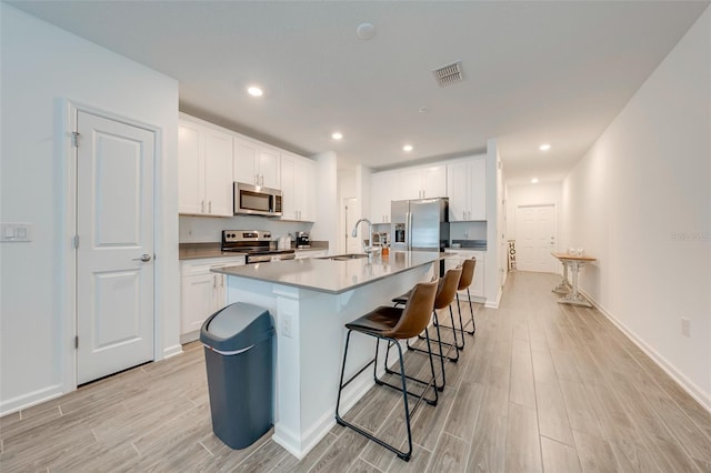 kitchen with sink, an island with sink, stainless steel appliances, white cabinets, and a breakfast bar area