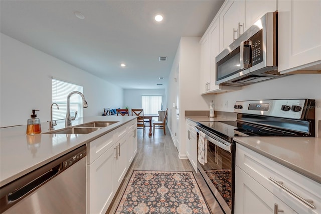 kitchen with sink, light hardwood / wood-style floors, appliances with stainless steel finishes, and white cabinetry