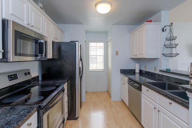 kitchen with appliances with stainless steel finishes, white cabinetry, dark stone countertops, and light hardwood / wood-style flooring