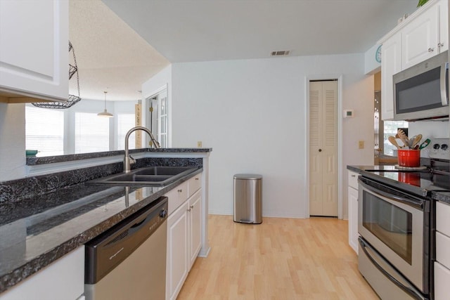 kitchen with white cabinets, pendant lighting, sink, appliances with stainless steel finishes, and light hardwood / wood-style flooring