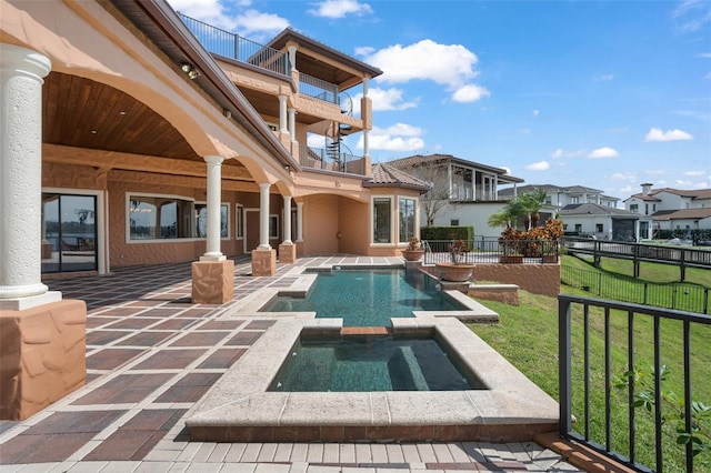 exterior space featuring a yard, a balcony, a swimming pool with hot tub, and a patio