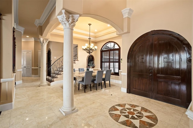 entrance foyer featuring light tile floors, crown molding, a tray ceiling, ornate columns, and a notable chandelier