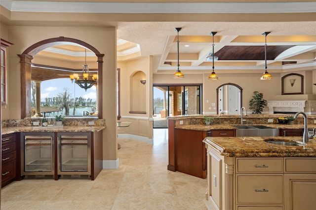 kitchen with a notable chandelier, hanging light fixtures, a raised ceiling, dark stone countertops, and sink