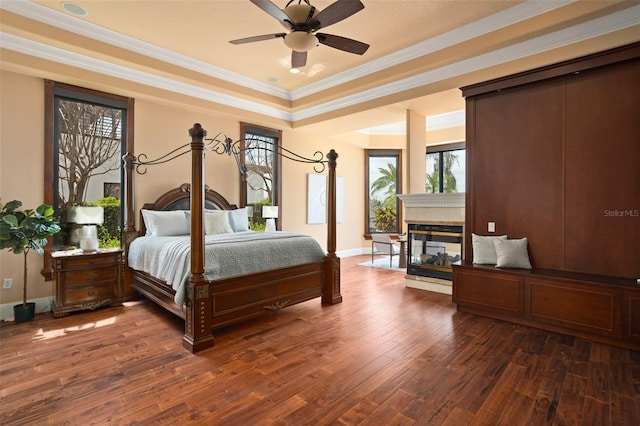 bedroom with ceiling fan, crown molding, a tray ceiling, a multi sided fireplace, and dark hardwood / wood-style flooring