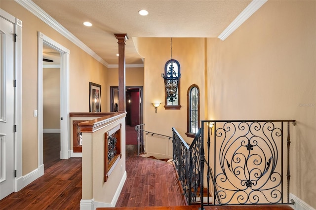 hallway with a textured ceiling, ornamental molding, decorative columns, and dark wood-type flooring