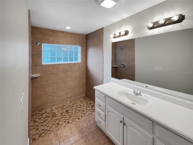 bathroom with a textured ceiling, tile flooring, vanity, and tiled shower