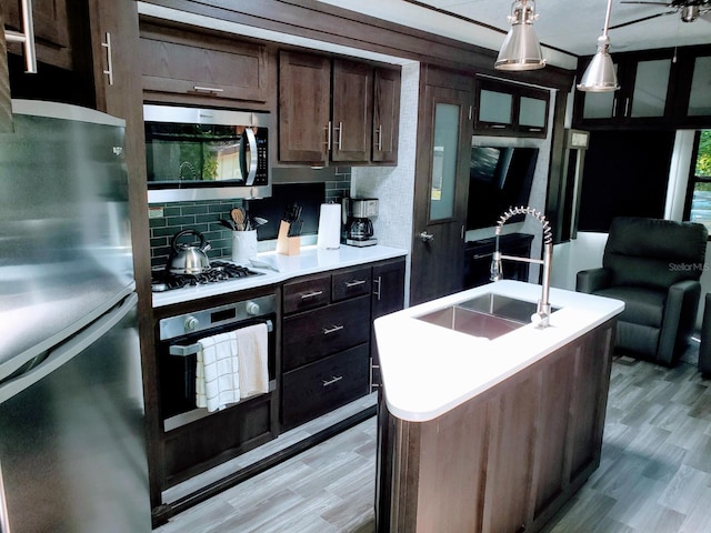 kitchen featuring appliances with stainless steel finishes, hanging light fixtures, a center island with sink, light hardwood / wood-style floors, and tasteful backsplash