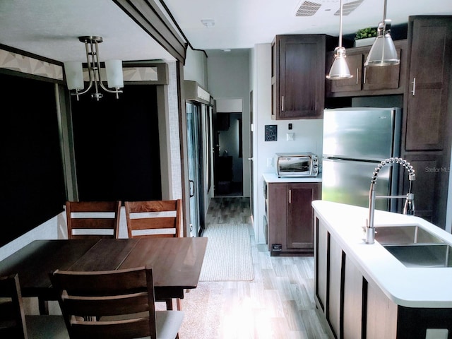 kitchen with dark brown cabinetry, a notable chandelier, stainless steel refrigerator, light wood-type flooring, and decorative light fixtures