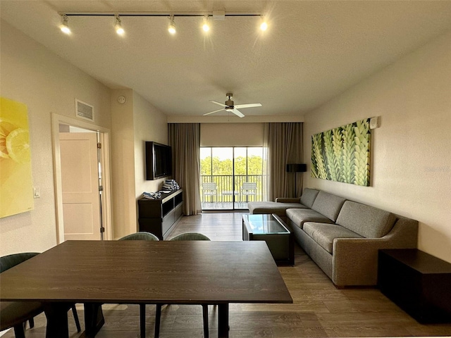 living room featuring a textured ceiling, dark wood-type flooring, rail lighting, and ceiling fan