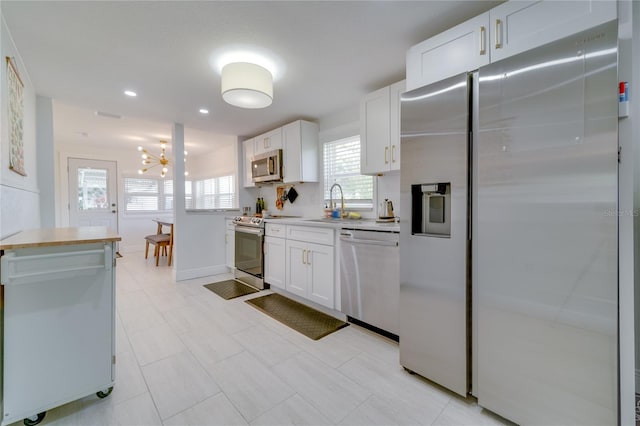 kitchen with a chandelier, stainless steel appliances, light tile floors, white cabinetry, and sink