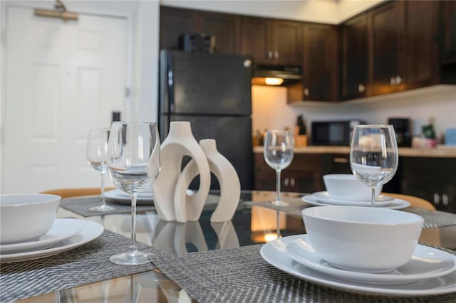 kitchen featuring dark brown cabinetry, black refrigerator, and wall chimney exhaust hood