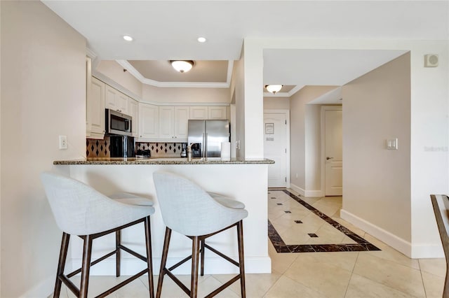 kitchen with stone countertops, a peninsula, stainless steel appliances, a kitchen bar, and light tile patterned floors