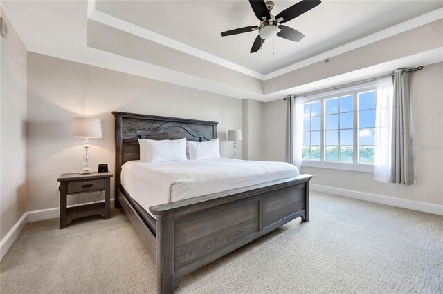 bedroom with baseboards, a raised ceiling, crown molding, and light colored carpet