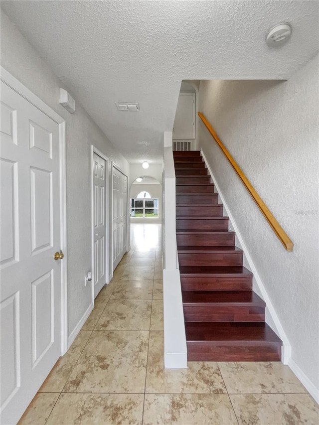 stairs with a textured ceiling and tile patterned flooring