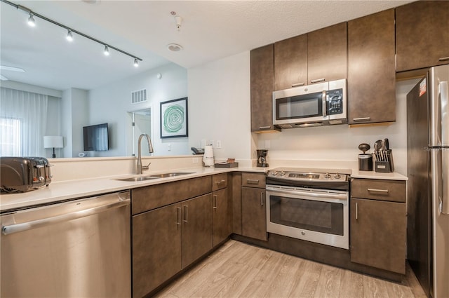 kitchen featuring kitchen peninsula, dark brown cabinets, appliances with stainless steel finishes, light wood-type flooring, and sink