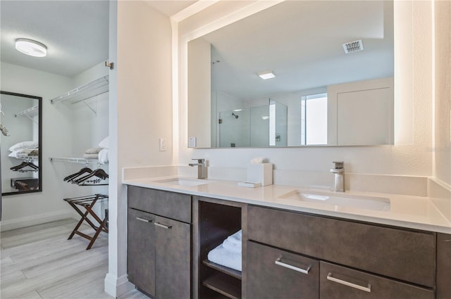 bathroom with double sink, a shower with shower door, vanity with extensive cabinet space, and hardwood / wood-style floors